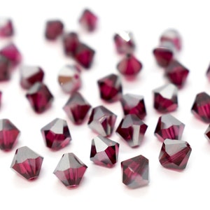 May include: A collection of faceted, dark red beads with a metallic sheen. The beads are scattered on a white surface, showcasing their geometric shapes and reflective qualities. Ideal for jewelry making or craft projects.
