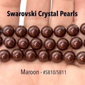 May include: A strand of maroon Swarovski Crystal Pearls. The pearls are round and have a glossy finish. The text "Maroon - #5810/5811" is printed below the pearls.