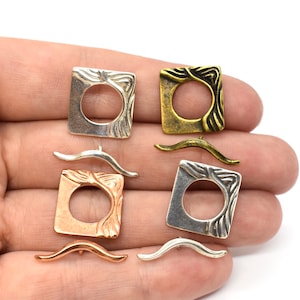 Puede incluir: Surtido de hallazgos de joyería de metal en tonos plata, oro y cobre. Cada hallazgo presenta un marco cuadrado con un círculo abierto en el centro y un diseño decorativo. También hay tres piezas de metal curvadas.