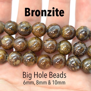 Puede incluir: Una hebra de cuentas de bronzita marrón y dorada con un agujero grande. Las cuentas son redondas y lisas, y están disponibles en tamaños de 6 mm, 8 mm y 10 mm.  Big Hole Beads.