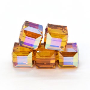 May include: A group of five iridescent amber glass beads, each with a square shape and a faceted design. The beads are stacked on top of each other, creating a pyramid shape.