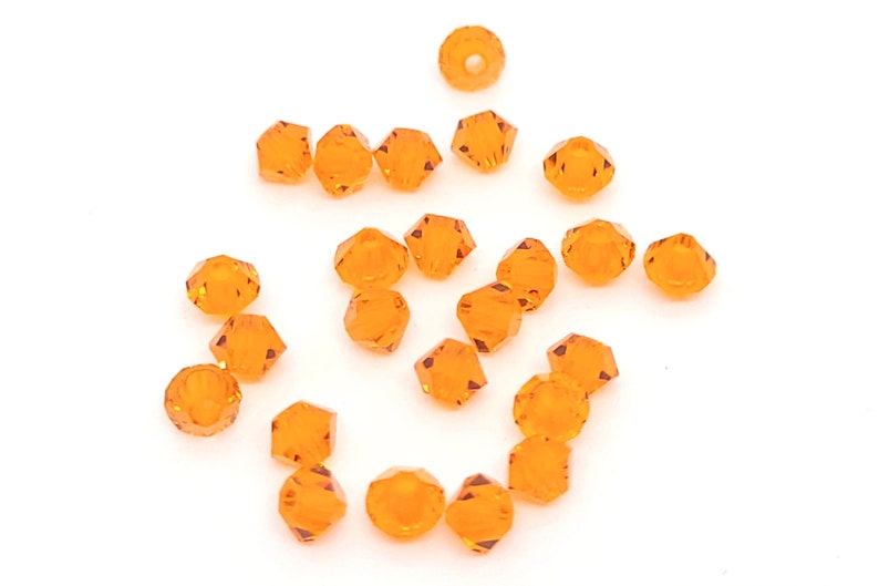 Puede incluir: Un grupo de peque&ntilde;as cuentas de vidrio facetadas de color naranja. Las cuentas est&aacute;n dispuestas en un patr&oacute;n aleatorio sobre un fondo blanco.