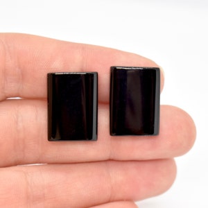 Peut inclure: Une paire de boucles d'oreilles rectangulaires noires. Les boucles d'oreilles sont lisses et brillantes.