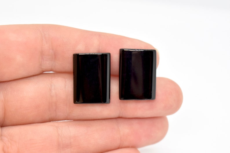 Peut inclure: Une paire de boucles d'oreilles rectangulaires noires. Les boucles d'oreilles sont lisses et brillantes.