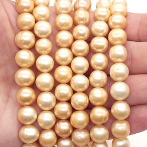 Könnte beinhalten: Eine Kette aus goldenen Perlen, jede Perle ist rund und glatt, mit einem dezenten Glanz. Die Perlen sind in einer Reihe angeordnet und bilden ein wunderschönes und elegantes Display.