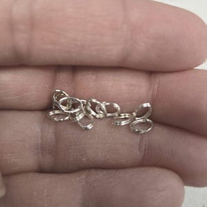 Puede incluir: Primer plano de un montón de anillas de salto plateadas, un tipo de hallazgo de joyería utilizado para conectar cadenas y otros componentes de joyería.