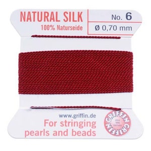 Puede incluir: Una bobina de hilo de seda natural rojo para enhebrar perlas y cuentas. La bobina está etiquetada con "NATURAL SILK" y "No. 6 100% Naturseide Ø 0,70 mm".