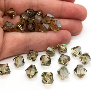 May include: A collection of green faceted glass beads. The beads are square shaped and have a slight iridescent sheen.