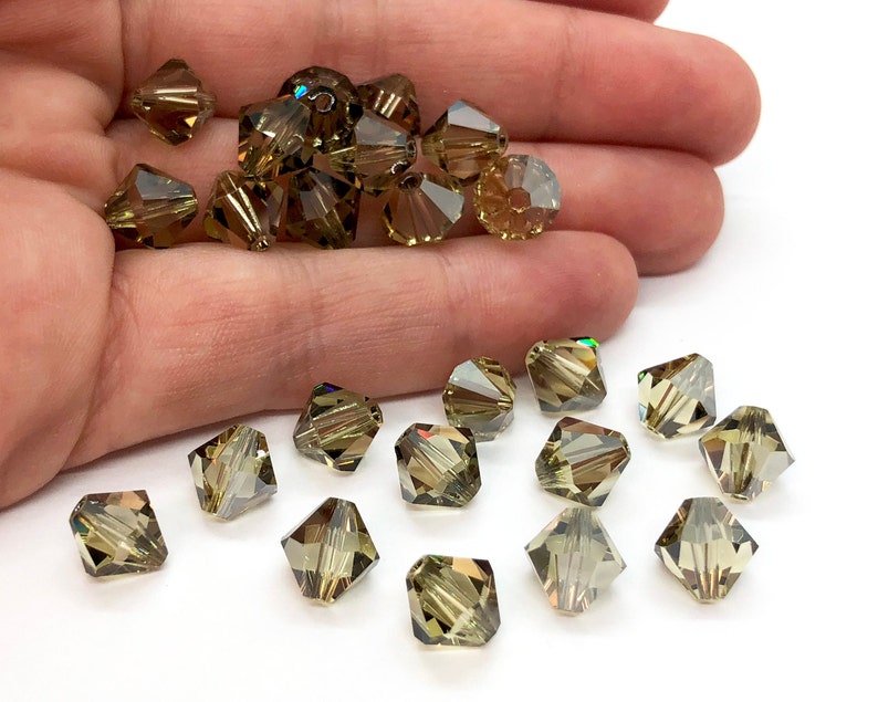 May include: A collection of green faceted glass beads. The beads are square shaped and have a slight iridescent sheen.