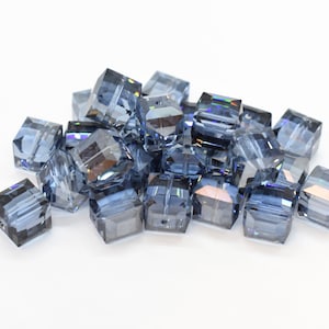 Könnte beinhalten: Ein Haufen dunkelgrauer quadratischer Glasperlen mit facettenreichem Finish. Die Perlen sind durchscheinend und haben einen leichten irisierenden Schimmer.