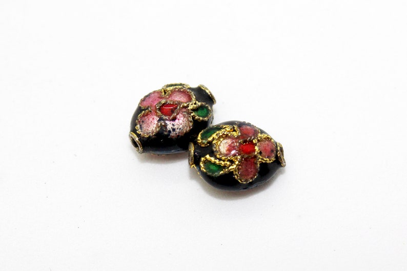 May include: Two black oval beads with gold trim and floral designs in pink, red, and green.