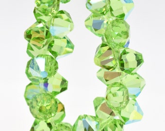 Può includere: Una fila di perline di vetro sfaccettate di colore verde chiaro. Le perline sono infilate su un filo trasparente e sono disposte in cerchio.