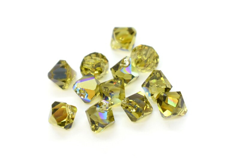 May include: A group of 12 iridescent green glass beads with a faceted square shape.