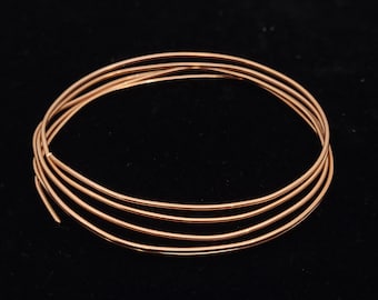 Puede incluir: Alambre de cobre enrollado, ideal para la fabricación de joyas y manualidades. El alambre es de color oro rosa cálido y está dispuesto en un patrón circular sobre un fondo negro. El alambre es fino y flexible, perfecto para diseños intrincados.