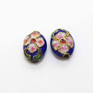 May include: Two oval-shaped beads with a blue enamel base and a floral design. The flowers are pink, white, and orange with gold accents.