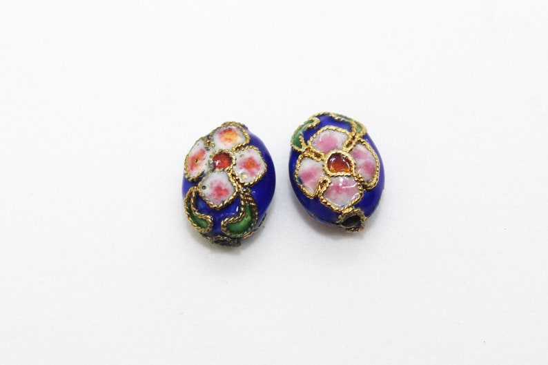 May include: Two oval-shaped beads with a blue enamel base and a floral design. The flowers are pink, white, and orange with gold accents.