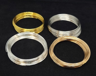 May include: Four circular coils of thin metal wire arranged in a square formation. Two coils are a bright gold tone, and two coils are a metallic silver tone. Each coil consists of multiple layered loops of wire, creating a uniform circular shape.