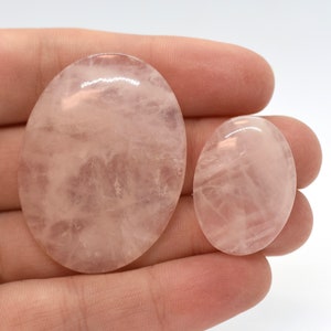 Pode incluir: Duas pedras de quartzo rosa de forma oval, uma maior que a outra, com uma cor rosa transl&uacute;cida e veios brancos. As pedras s&atilde;o lisas e polidas.