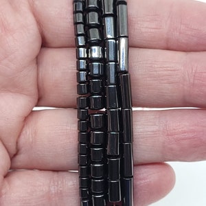 May include: A strand of black and silver hematite beads. The beads are various sizes and shapes, including round, square, and rectangular.