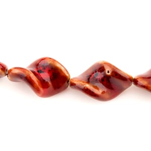 May include: A strand of red and brown ceramic beads with a twisted, wavy design.