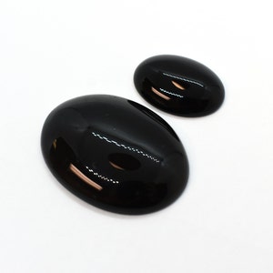 May include: Two black oval-shaped gemstones, one larger than the other, on a white background.