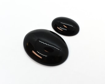 May include: Two black oval-shaped gemstones, one larger than the other, on a white background.