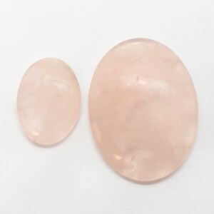 Pode incluir: Duas pedras de quartzo rosa lisas de forma oval. A pedra maior &eacute; rosa claro e a pedra menor &eacute; de um tom rosa ligeiramente mais escuro.