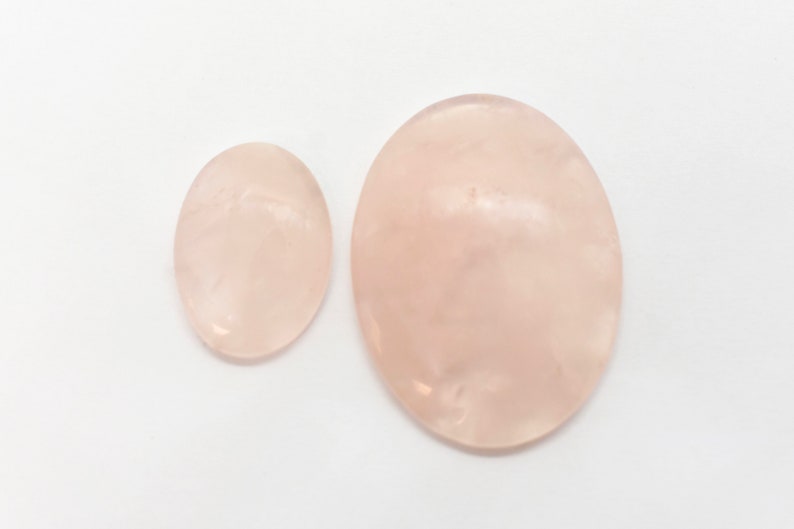Pode incluir: Duas pedras de quartzo rosa lisas de forma oval. A pedra maior &eacute; rosa claro e a pedra menor &eacute; de um tom rosa ligeiramente mais escuro.
