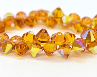 Può includere: Una collana di perline di vetro sfaccettate di colore ambrato. Le perline sono infilate su un filo trasparente e hanno un leggero bagliore iridescente.
