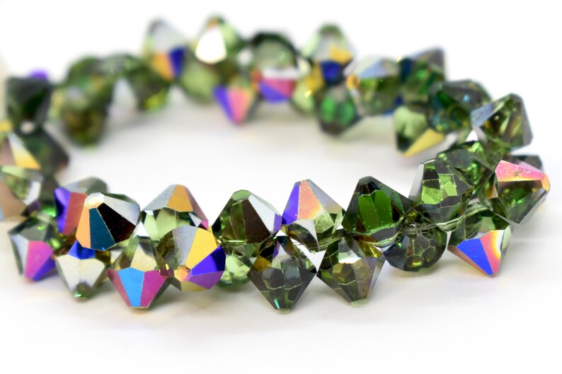 May include: A strand of green faceted crystal beads with iridescent rainbow accents. The beads are strung on a clear thread.