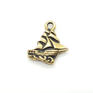 May include: Gold-toned metal charm shaped like a sailboat with a detailed design. The charm has a loop at the top for attaching to a necklace or bracelet.