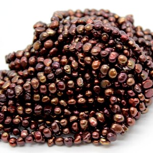 Może przedstawiać: Sznur brązowych pereł słodkowodnych z iryzującym połyskiem. Perły są nieregularne pod względem kształtu i rozmiaru, tworząc unikalny i fakturowany wygląd.