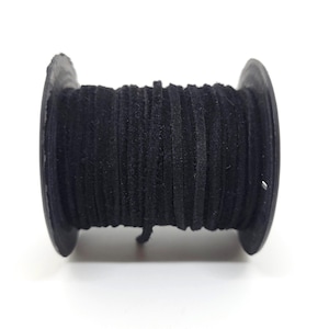 May include: A spool of black suede leather cord. The cord is tightly wound around a black plastic spool. The suede appears soft and has a matte finish. The spool is set against a white background.