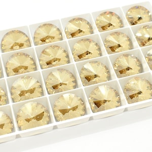 May include: A white tray filled with 20 round, clear, faceted, light gold rhinestones.