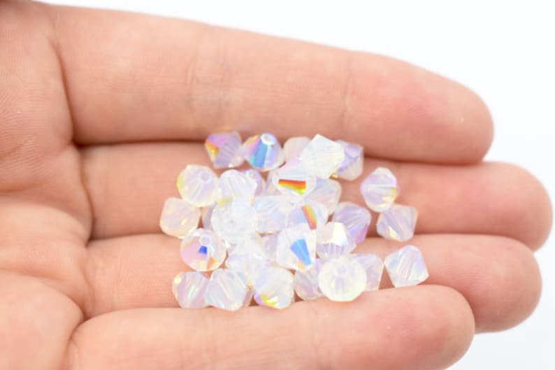 May include: A handful of iridescent, faceted beads in various shapes. The beads are primarily white with a subtle rainbow sheen, reflecting light. These beads are suitable for jewelry making and crafting.