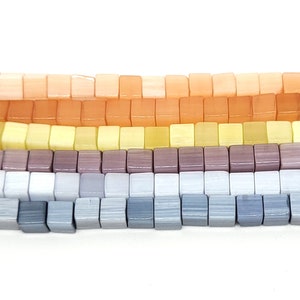 May include: A strand of square-shaped beads in a gradient of colors, starting with peach, transitioning to yellow, then to purple, and finally to gray.