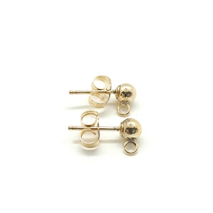 May include: Two pairs of gold-colored ball stud earrings. Each earring features a small, round ball on a post with a loop for attaching charms or other decorative elements. The earrings are set against a white background.