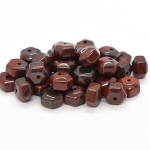 May include: A pile of approximately 30 dark red and black gemstone beads. The beads are faceted and have a hole drilled through the center. The beads are arranged in a loose pile on a white background.