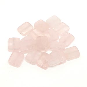 May include: A collection of translucent, pale pink rose quartz beads. The beads are rectangular with rounded corners and appear tumbled. The beads are scattered on a white background.