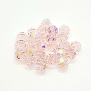 K&ouml;nnte beinhalten: Eine Ansammlung facettierter, hellrosa Kristallperlen. Die Perlen haben eine irisierende Qualit&auml;t und reflektieren mehrere Farben. Die runden Perlen scheinen aus Glas oder Kristall zu bestehen und eignen sich f&uuml;r Schmuckherstellung oder Bastelarbeiten.