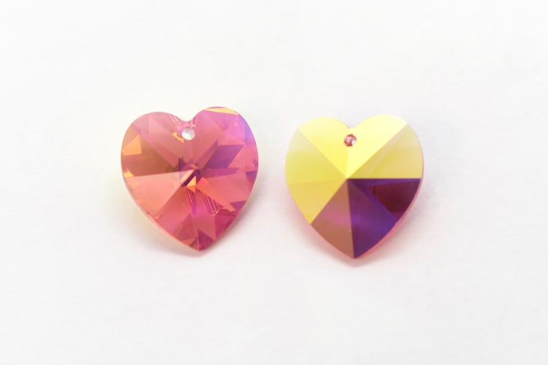 Puede incluir: Dos abalorios de cristal en forma de coraz&oacute;n, uno de color iridiscente rosa y morado y el otro de color iridiscente amarillo y morado.