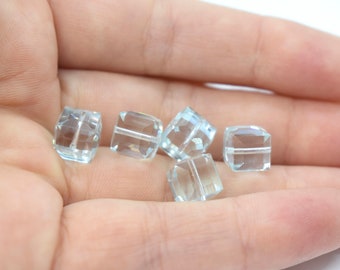 May include: Six clear, faceted, square-shaped beads made of aquamarine. The beads are approximately 1 cm in size and have a hole drilled through the center.