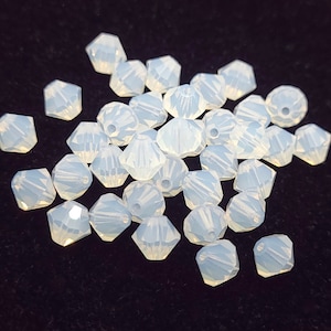 May include: A pile of white iridescent glass beads, each bead is faceted and has a hexagonal shape.