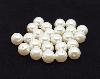 May include: A collection of small, round, off-white faux pearl beads. Each bead features a smooth, glossy surface and a single central hole for threading. The beads are arranged in a cluster, showcasing their uniform spherical shape and creamy color.