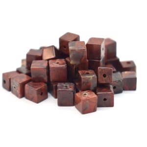 May include: A pile of brown and red jasper gemstone beads, each bead is a cube with a hole drilled through the center.