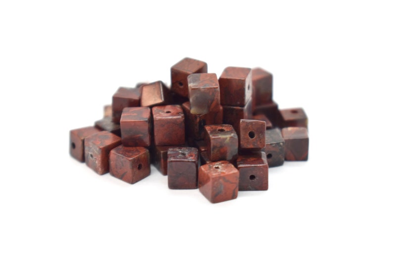 May include: A pile of brown and red jasper gemstone beads, each bead is a cube with a hole drilled through the center.