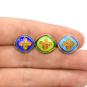 May include: Three square-shaped enamel buttons with gold trim and a gold floral design. The buttons are blue, green, and light blue.