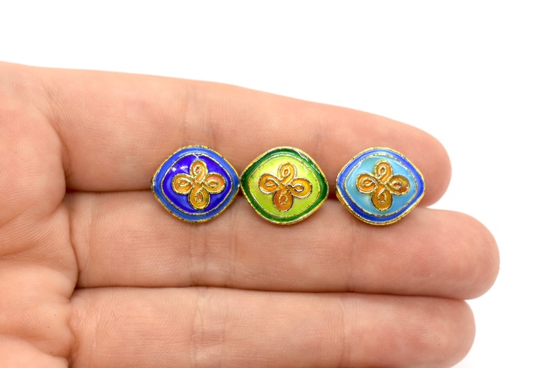 May include: Three square-shaped enamel buttons with gold trim and a gold floral design. The buttons are blue, green, and light blue.