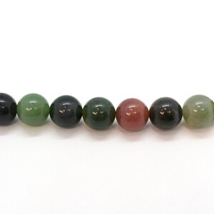May include: A strand of round, green, black, and pink agate beads. The beads are all approximately the same size and are strung on a clear thread.