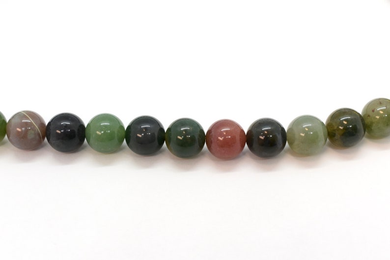 May include: A strand of round, green, black, and pink agate beads. The beads are all approximately the same size and are strung on a clear thread.